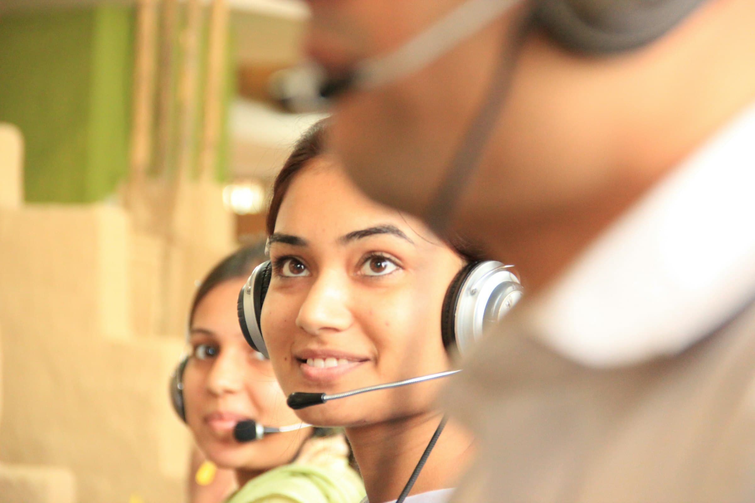 A call handler wearing a headset, smiling as she listens, with colleagues on the same row beside her.